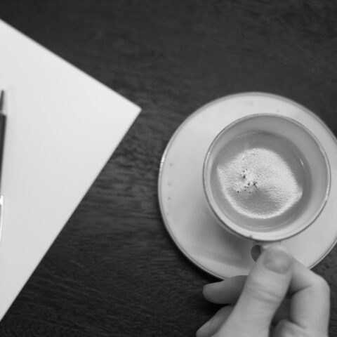 Intellecta merkt mappa og penni merktur Intellecta. Kvenmannshönd heldur í kaffibolla með kaffi með froðu